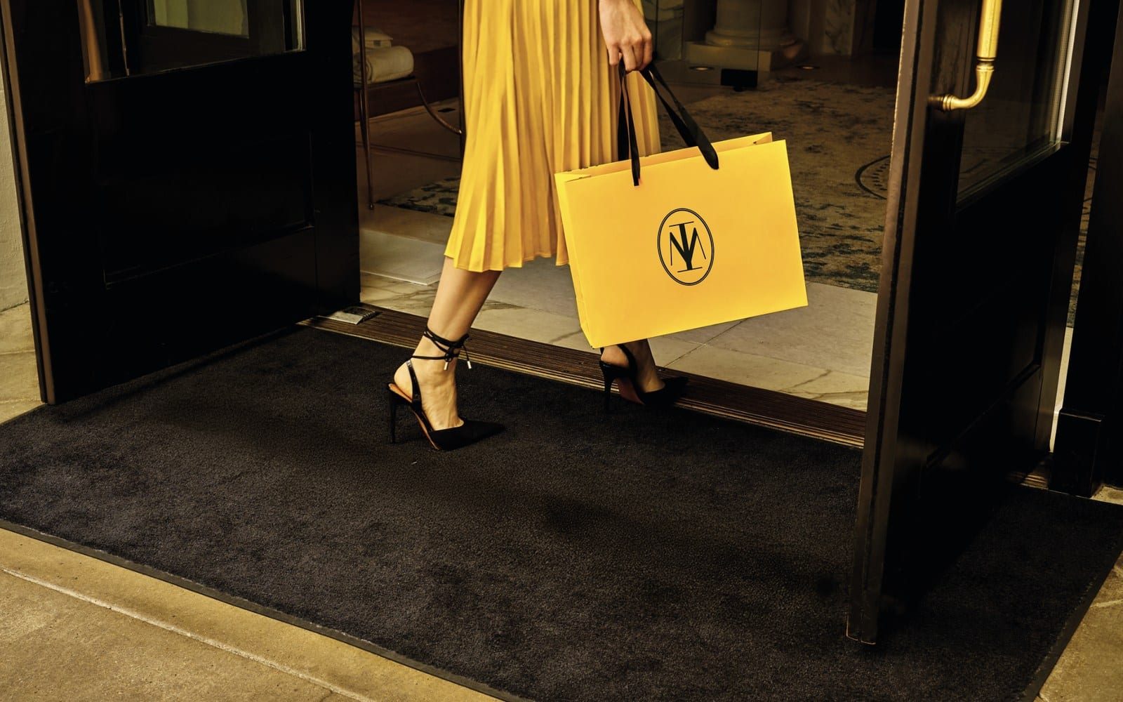 Gele draagtas met het ovale monogram van Meerduyn, gedragen in een hotelentree